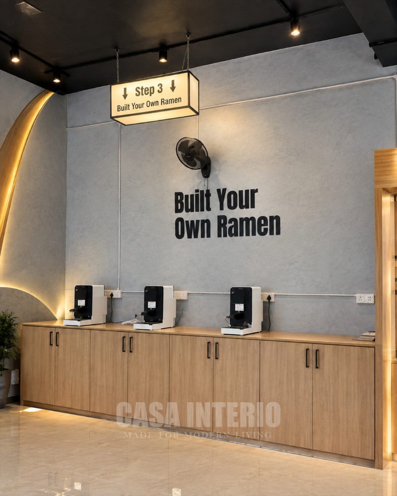 Self-serve ramen station on oak cabinetry under a lit hanging sign